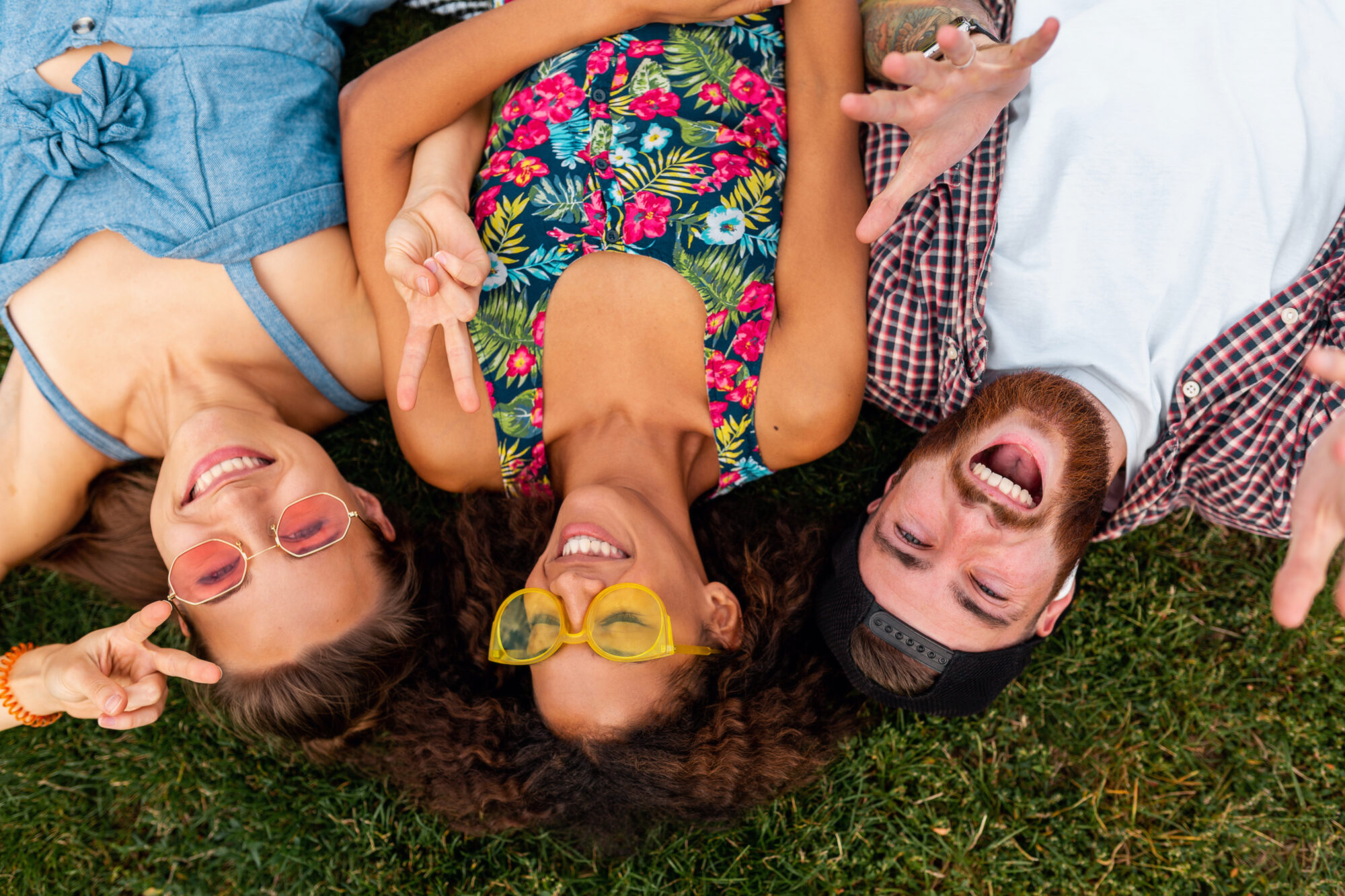 top view from above on colorful stylish happy young company of friends lying on grass in park, man and women having fun together, summer hipster fashion style, traveling smiling and positive